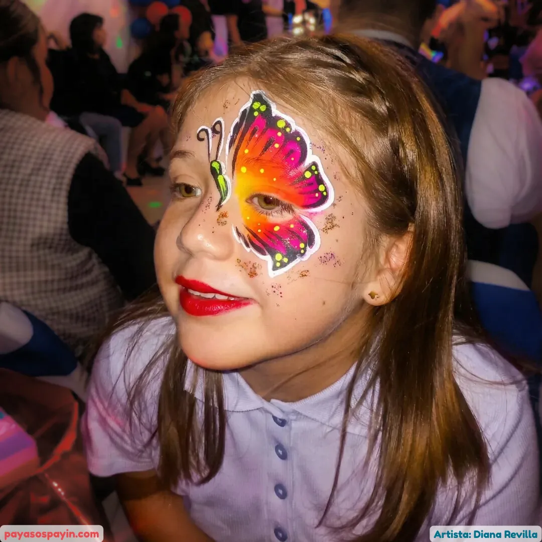 Niña con pintacaritas de mariposa multicolor en tonos cálidos y glitter en fiesta infantil