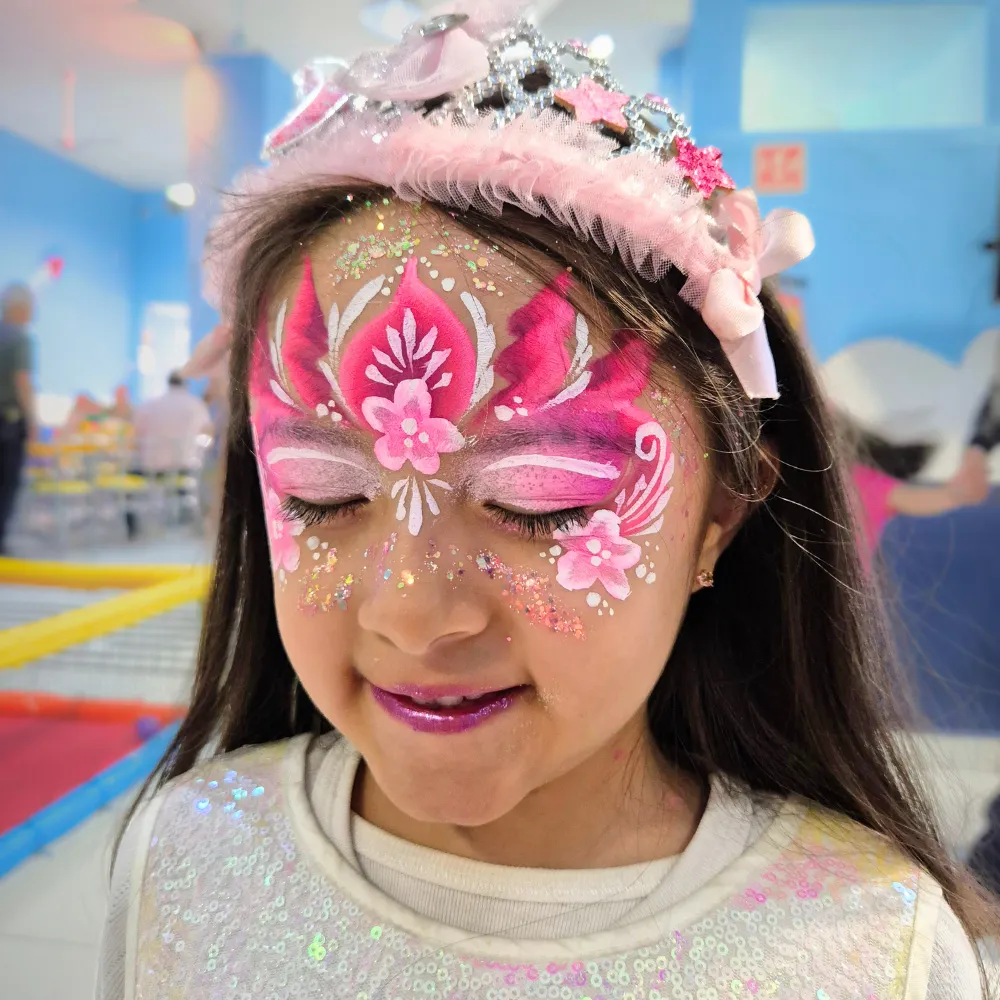 Niña con ojos cerrados mostrando maquillaje de corona de princesa rosa con flores y glitter