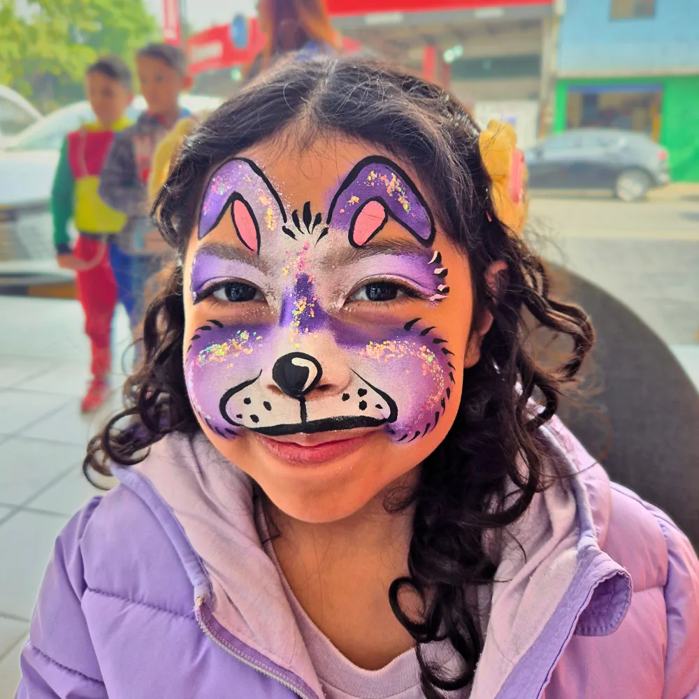 Pintacaritas de perrita de fantasía en tonos lila y morado con glitter para niñas en fiestas infantiles CDMX y EDOMEX
