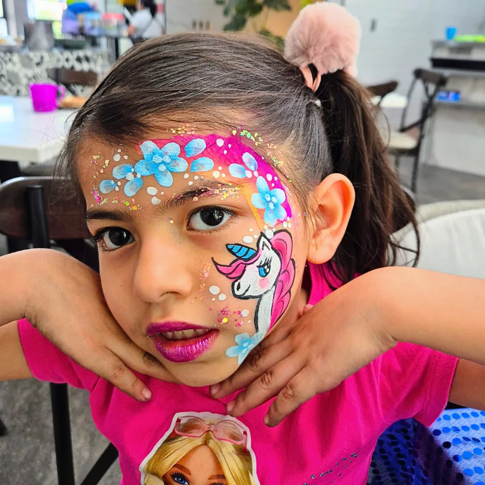 Pintacaritas de unicornio mágico con flores celestes, arcoíris One Stroke y glitter para niñas en fiestas CDMX