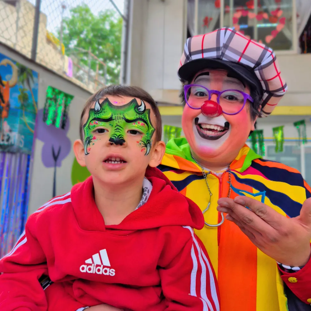 Niño con pintacaritas de dinosaurio verde junto al Payaso Payín en fiesta infantil CDMX y EDOMEX