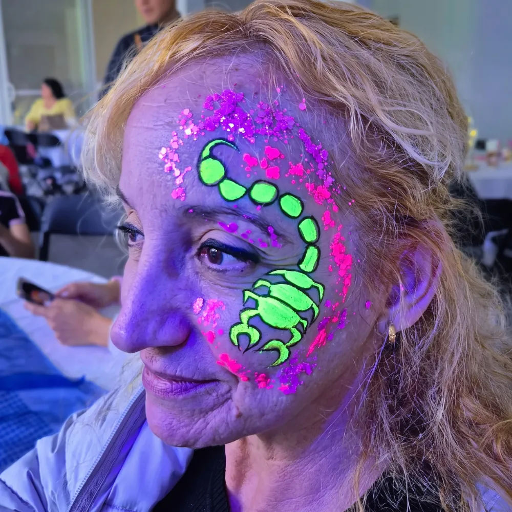 Mujer adulta con pintacaritas de escorpión fluorescente reactivo a luz negra UV con glitter neón en CDMX