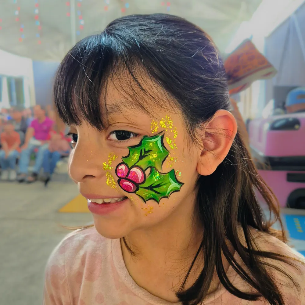 Pintacaritas de hojas de muérdago navideño con cerezas y destellos dorados en mejilla para niñas en CDMX y EDOMEX