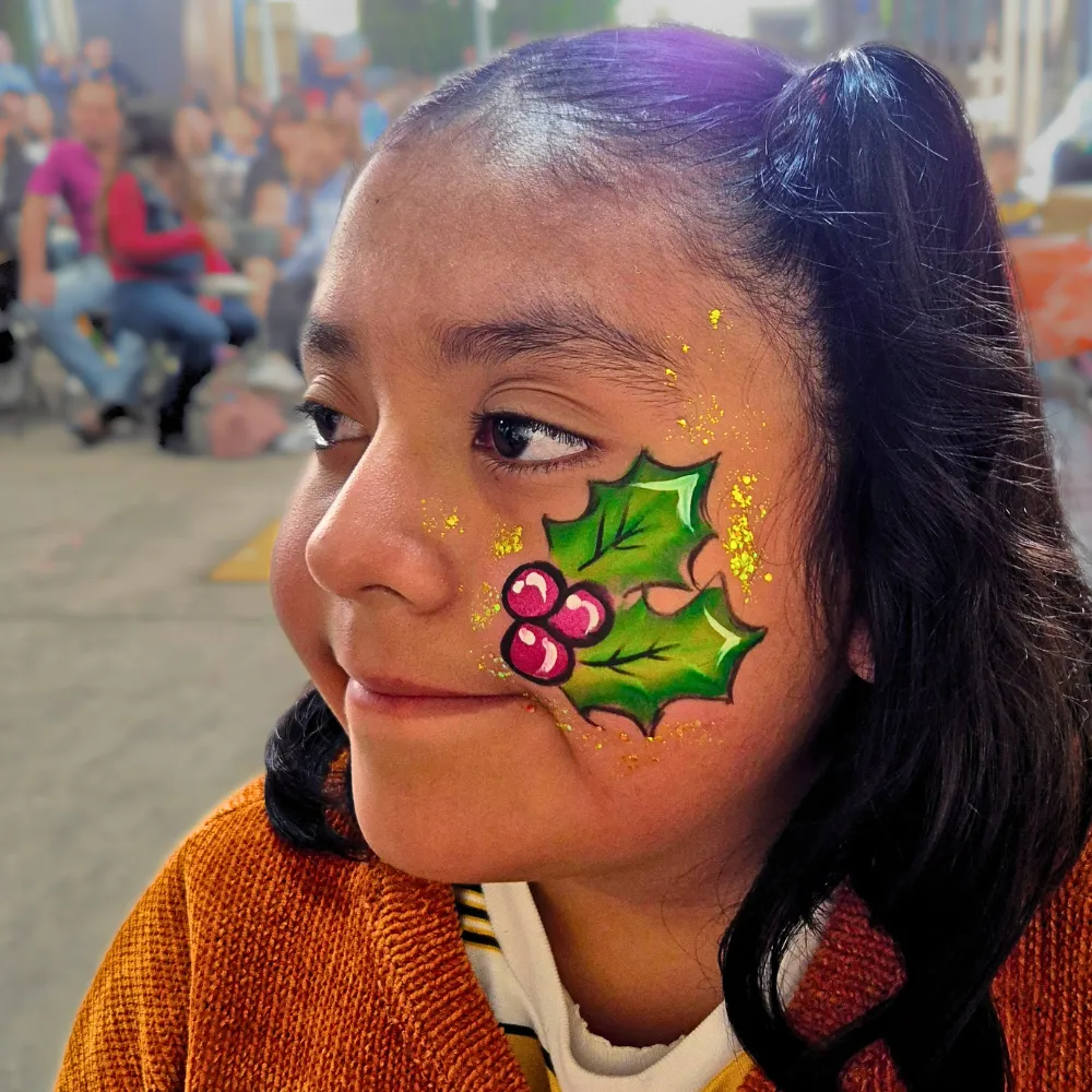 Pintacaritas de muérdago navideño con hojas verdes cerezas y glitter dorado en mejilla para niñas en CDMX y EDOMEX