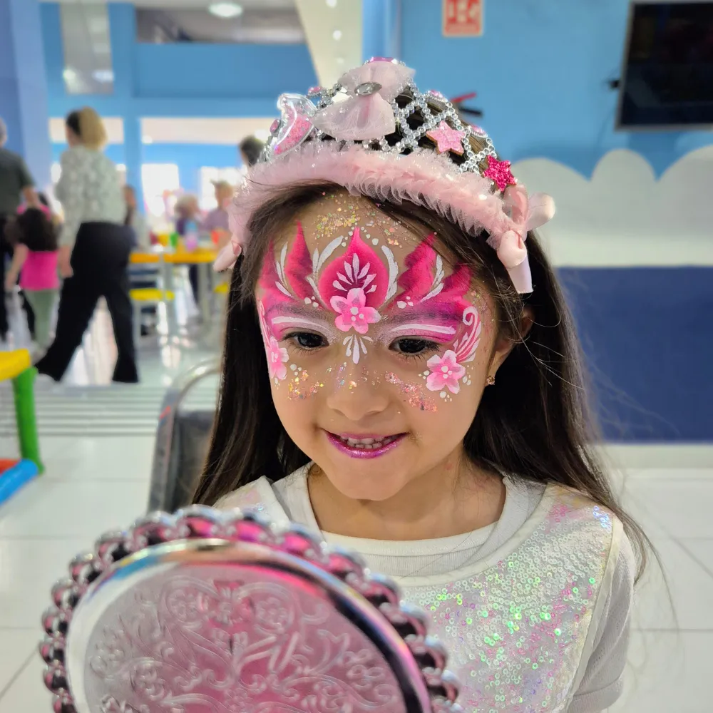Niña con corona de princesa rosa y tiara física sonriendo al verse en un espejo de mano