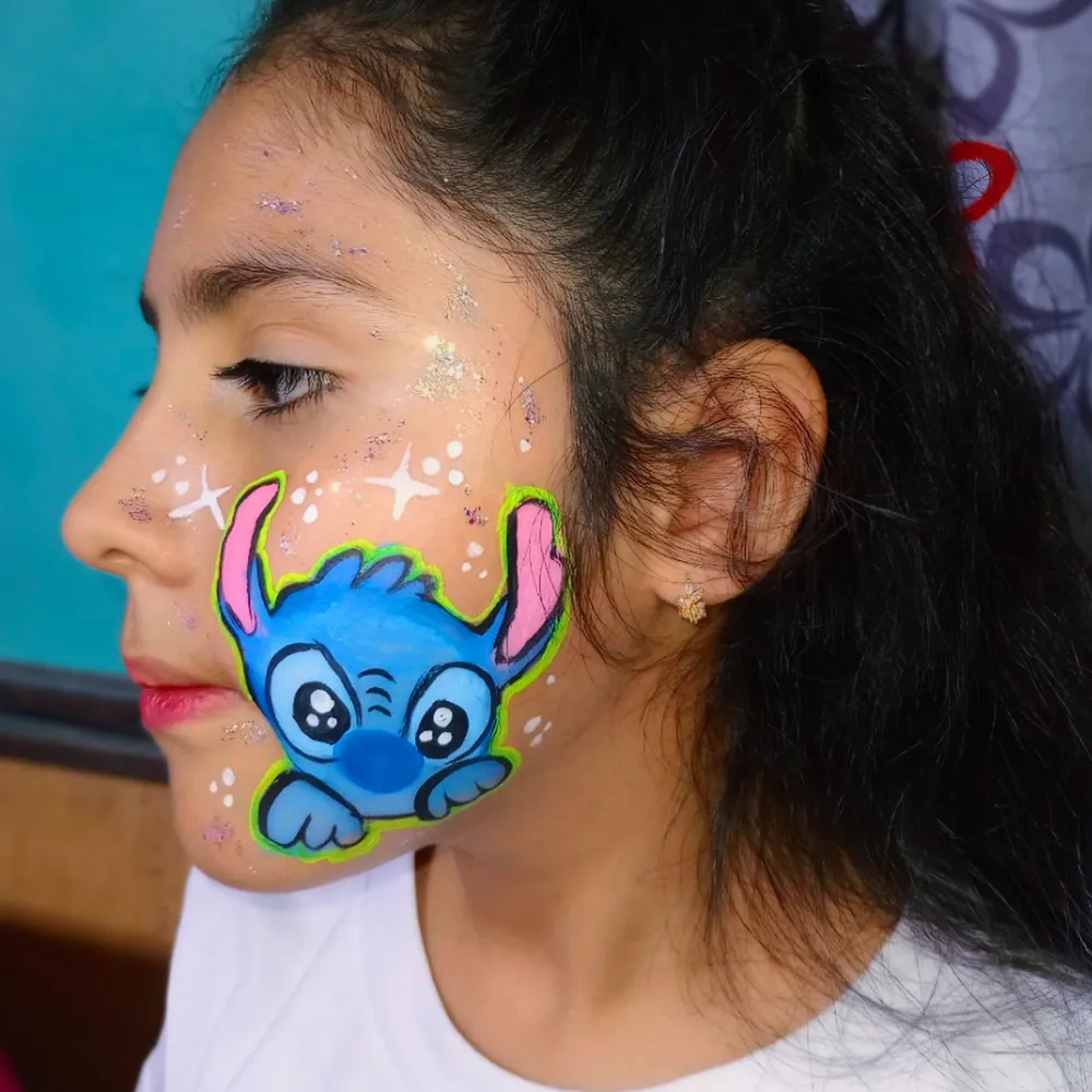 Pintacaritas de Stitch tierno kawaii asomándose en mejilla con destellos y glitter para niñas en CDMX y EDOMEX